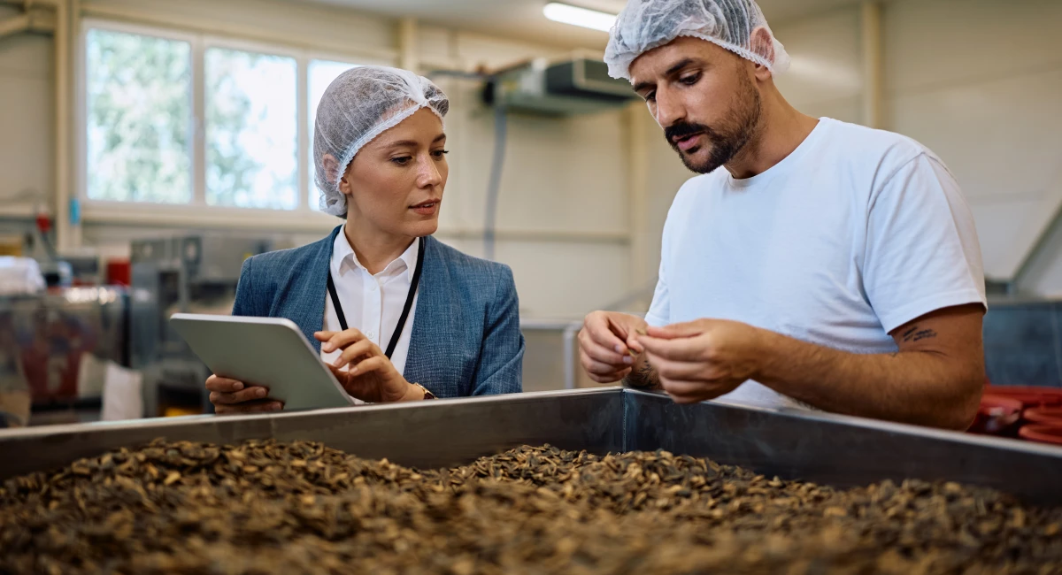 Food processing plant manager and worker examining containers with sunflower seeds.