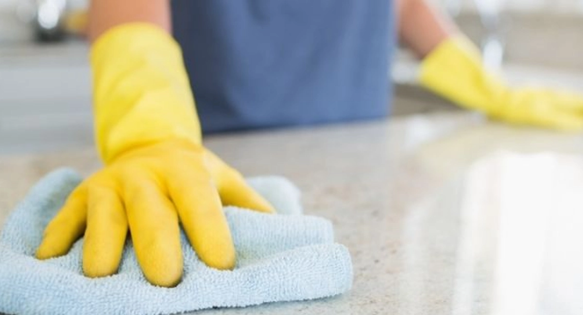 Man wearing yellow gloves cleans kitchen counters with blue towel.