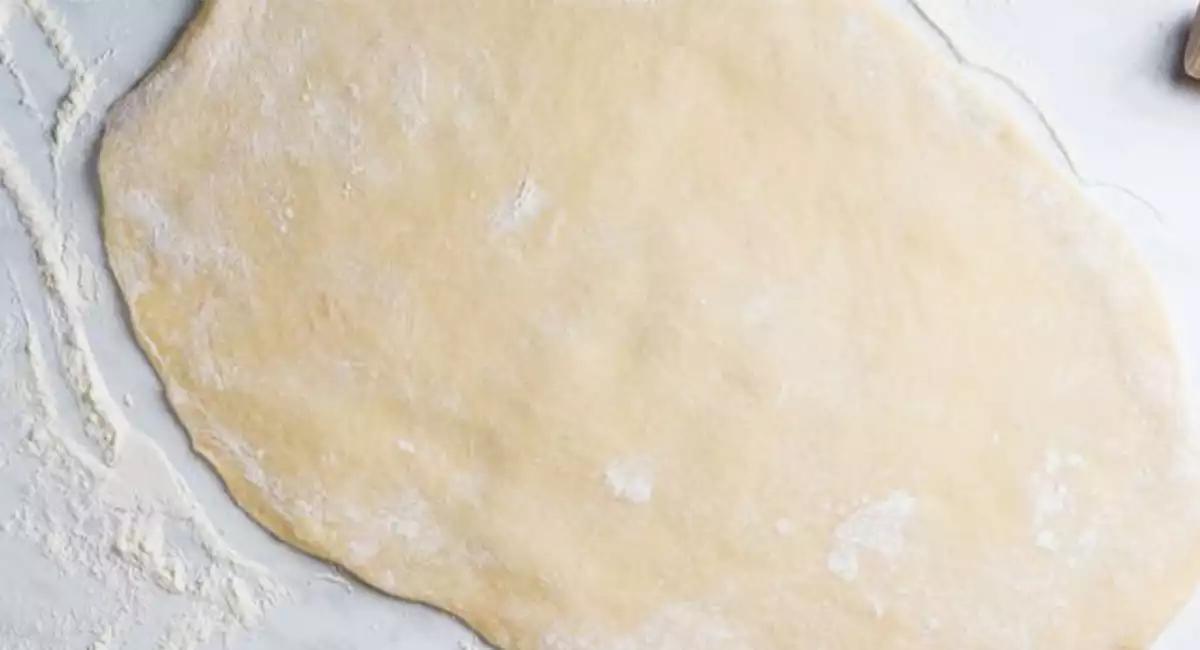 Pastry dough covered in flour rolled out next to a rolling pin on a baking counter.