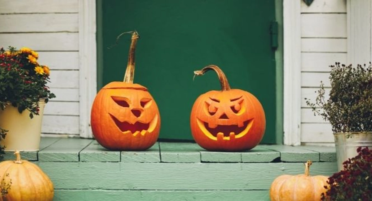 Two jack o lanterns with spooky faces on porch of house