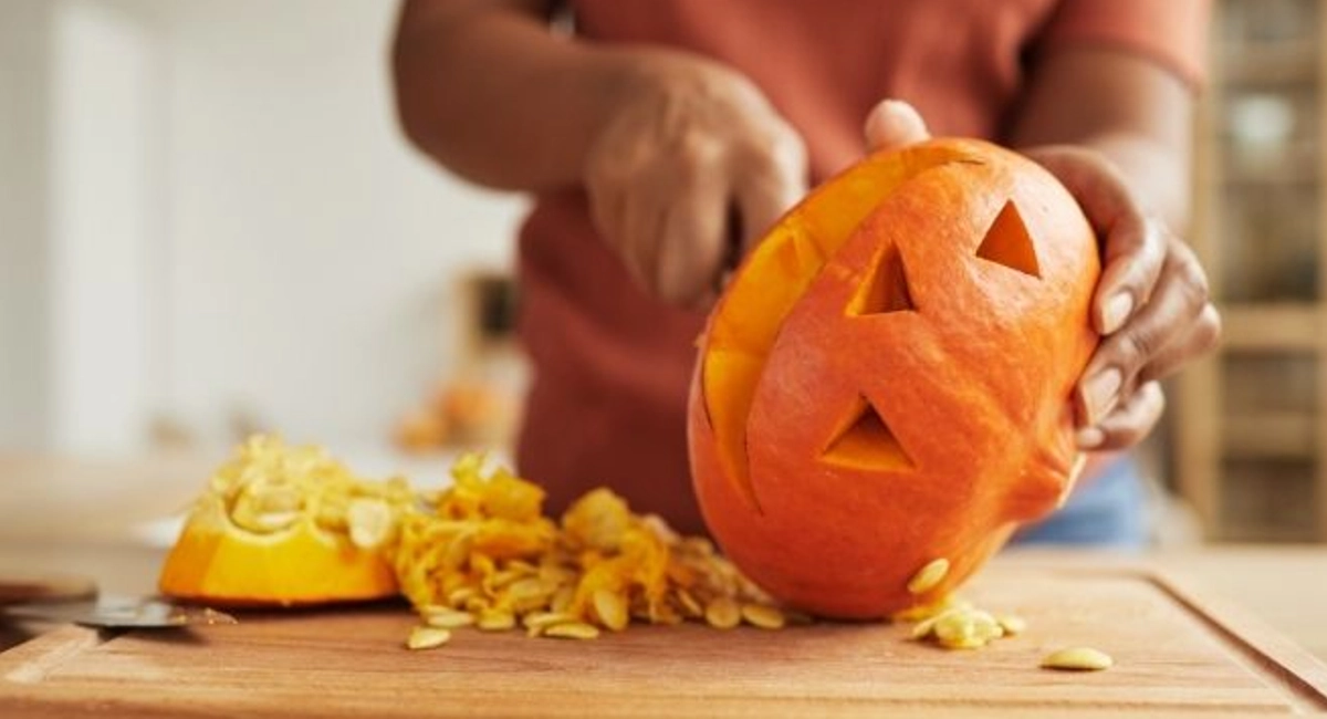 Woman standing at table carving Jack-O'-Lantern out of ripe orange pumpkin