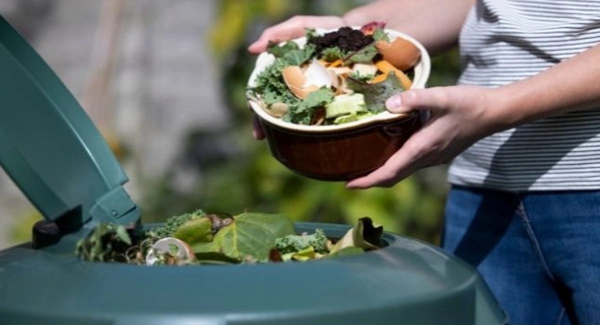Man throwing food scraps into green compost bin.