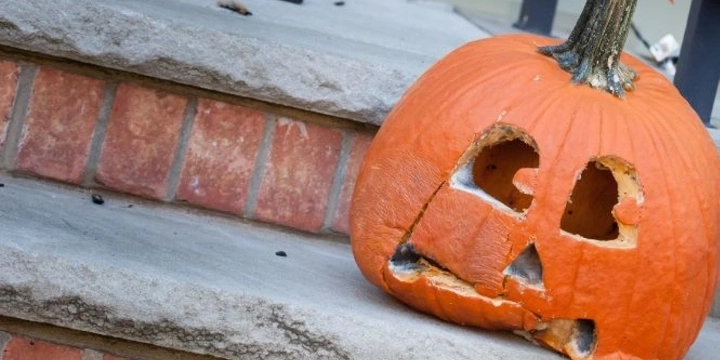 A moldy, decaying jack-o-lantern sits on someone's front steps after Halloween.
