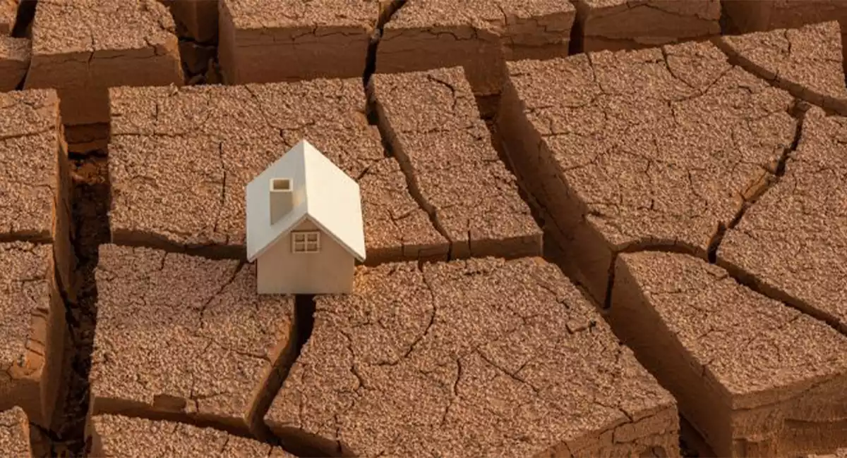 A wooden symbolic house stands on the cracked red clay in the desert