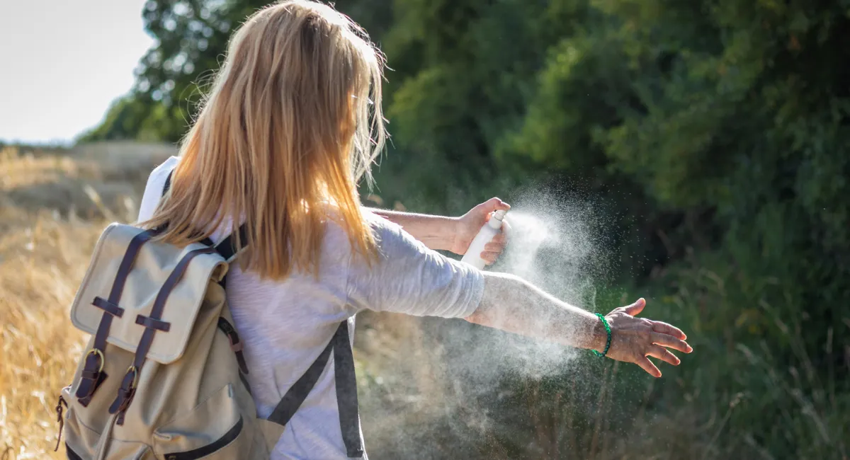 woman spraying bug repellent in an outside area