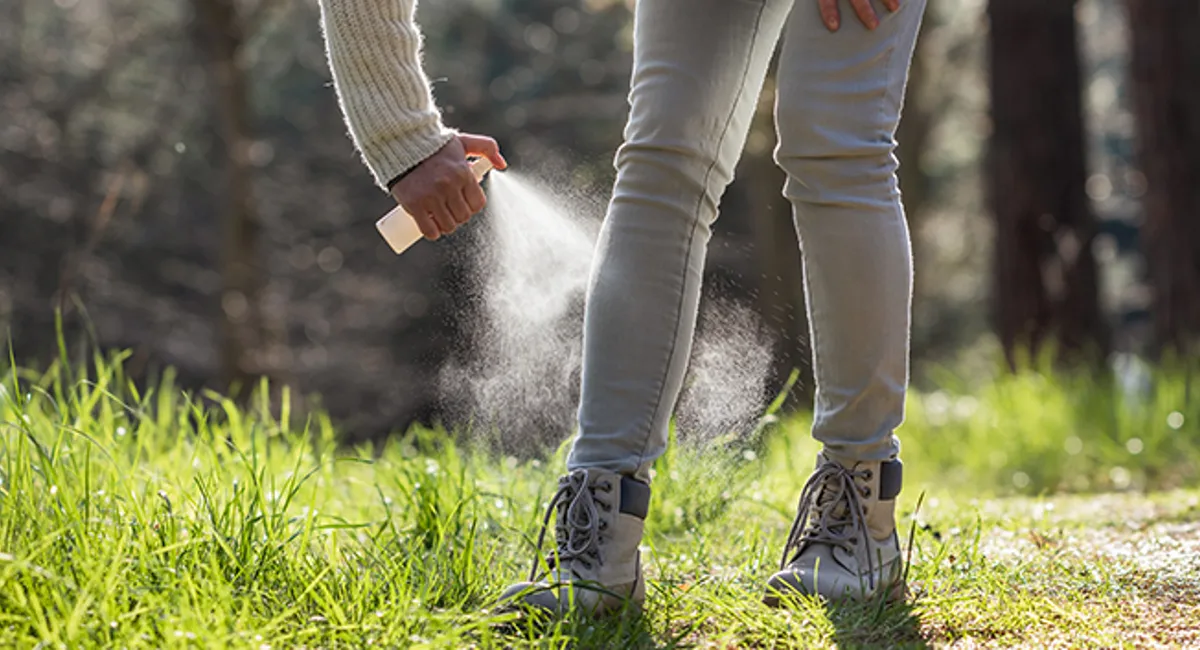 Person applying mosquito repellent while outside near woods