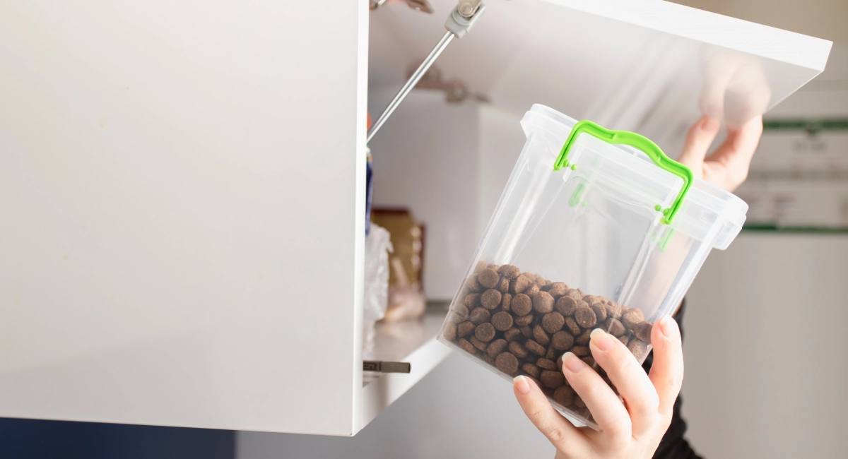 A person places a sealed tub of pet food into a cupboard
