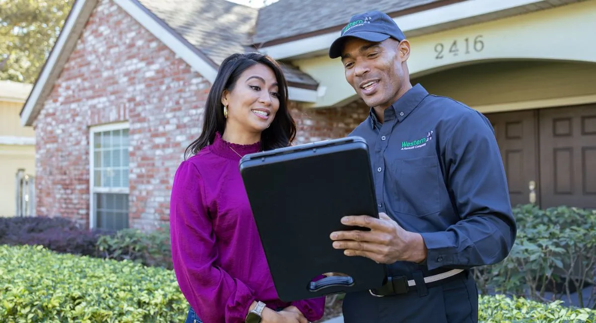 Western exterminator colleague with customer reading from tablet